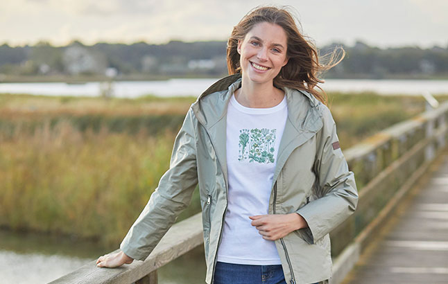 Frau im Parka mit T-Shirt vor Strand-Kulisse